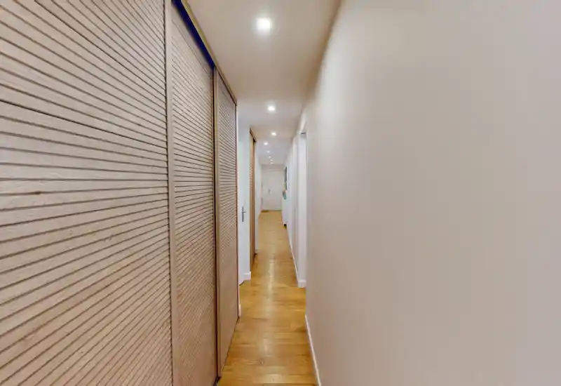 Couloir étroit et lumineux avec sol en bois et portes de placard intégrées; éclairage encastré au plafond pour un couloir d'entrée moderne et soigné.