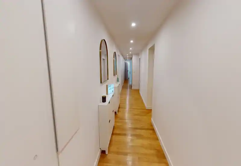 Long couloir lumineux avec un sol en bois, spots encastrés au plafond et une console fine avec miroirs — idéal comme dégagement d'entrée reliant les pièces.