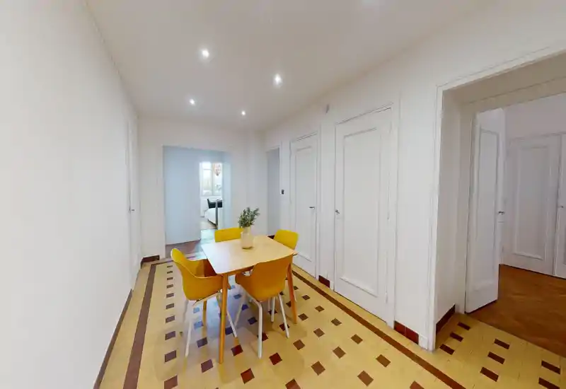 Coin repas compact avec une table en bois et quatre chaises jaunes sur un sol carrelé décoratif ; murs neutres et éclairage encastré au plafond créent un espace propre et accueillant, parfait pour des repas décontractés.