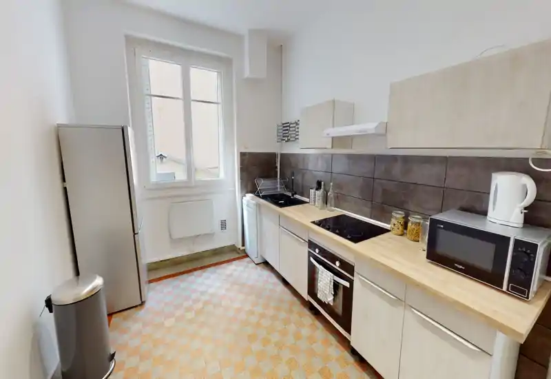 Cuisine compacte et lumineuse avec plan de travail en bois, plaque à induction, four et grand réfrigérateur. Agencement propre et fonctionnel, parfait pour les locations.