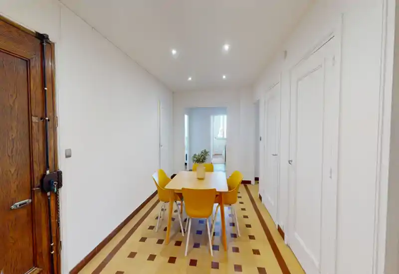Coin repas lumineux et bien composé avec une table en bois et quatre chaises jaunes sur un sol carrelé décoratif ; spots encastrés et vase central créent une ambiance accueillante.