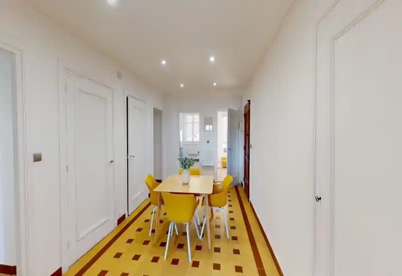Espace repas lumineux et bien agencé avec une table en bois et six chaises jaunes sur un sol carrelé à motifs ; une décoration discrète et des spots au plafond créent une ambiance chaleureuse pour les repas.
