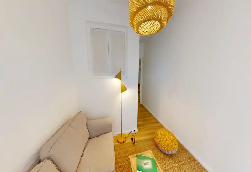 Petit salon chaleureux avec canapé beige, tapis tressé et luminaires en rotin; un coin accueillant pour se détendre ou lire.