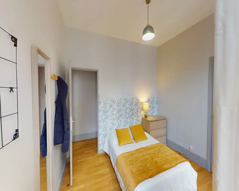 Sunny, well-staged single bedroom with a neatly made bed, warm mustard textiles and a bedside lamp that creates a cozy atmosphere.