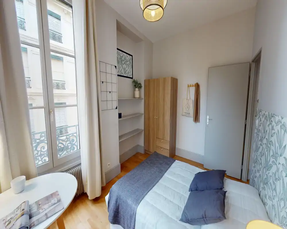 Dormitorio luminoso y con estilo, con ventana grande, cama doble con ropa de cama neutra y cojines decorativos, armario y estanterías — perfecto para una estancia urbana acogedora.