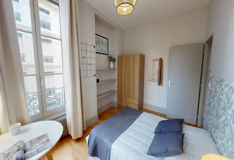 Bright, stylish bedroom with a large window, double bed dressed in neutral linens and decorative cushions, plus a wardrobe and shelving — ideal for a cozy urban stay.
