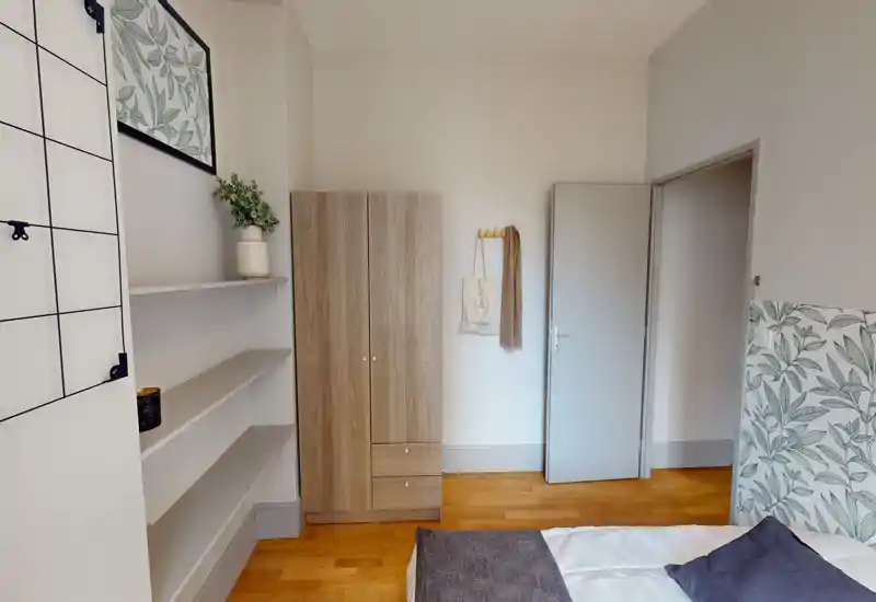Neatly staged bedroom with a visible bed corner, patterned headboard and a wooden wardrobe; bright, calm and ready for guests.