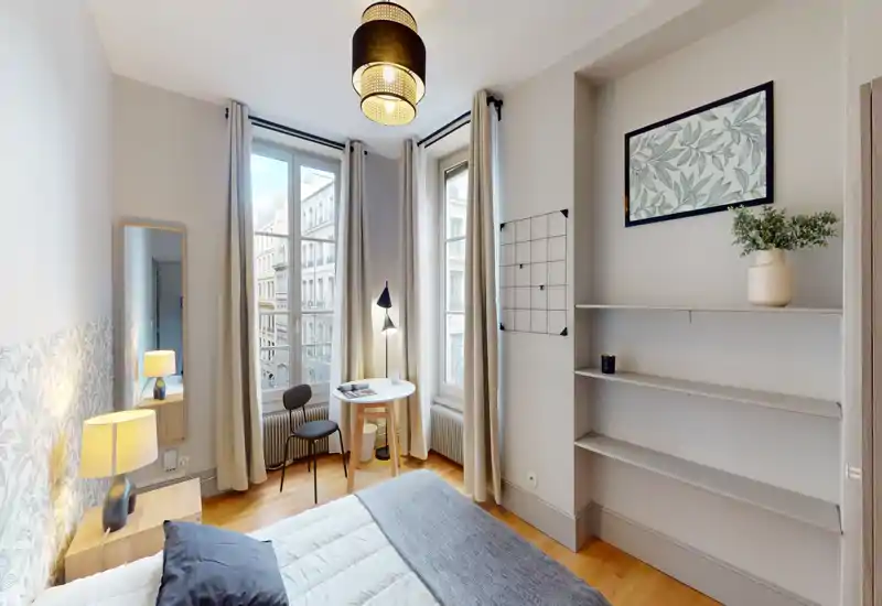 Bright, stylish bedroom with a double bed, bedside table and large windows that bring abundant natural light. Neutral tones, tasteful wall art and a small table create a calm, inviting space ideal for short-term rentals.