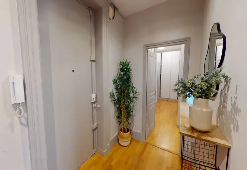 Entrée lumineuse et accueillante avec porte d'entrée sécurisée, sol en bois, console décorative et miroir — un espace de transition soigné vers le reste de l'appartement.