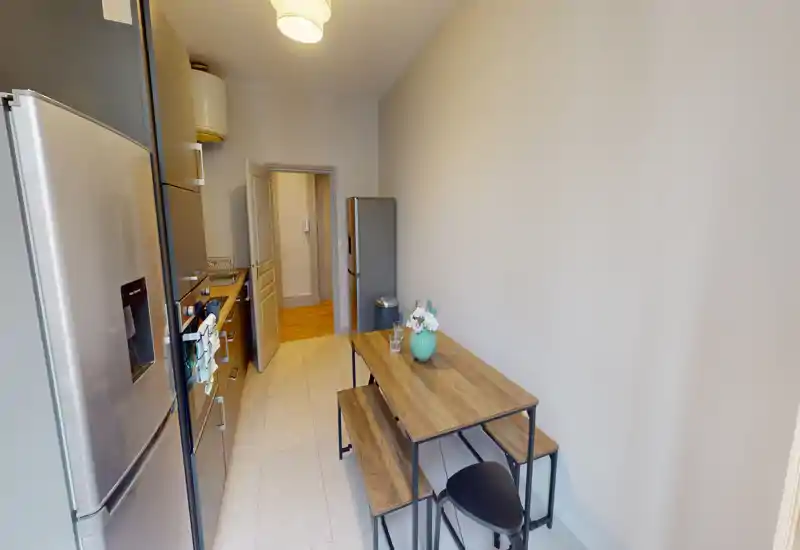 Narrow modern kitchen with stainless appliances and a wooden dining table for two; bright, tidy and efficiently arranged for small-space living.