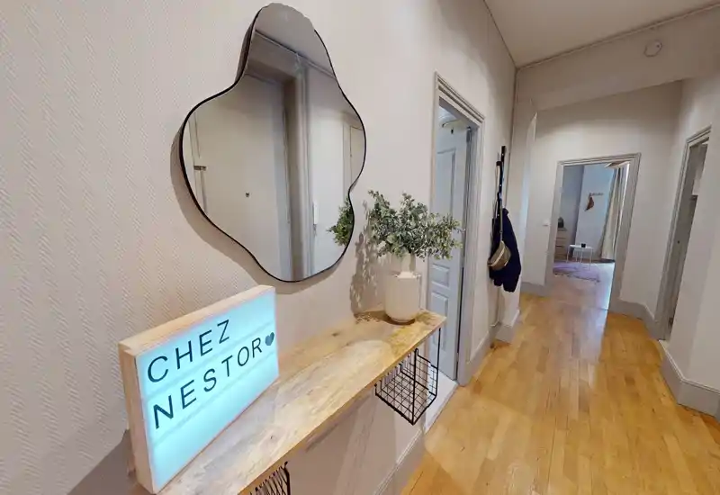 Entrée lumineuse et accueillante avec console en bois, miroir décoratif et boîte lumineuse; parquet poli et perspective dégagée sur les pièces adjacentes.