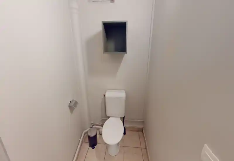 Petit WC lumineux avec toilette compacte, niche murale et sol carrelé ; espace simple et soigné, adapté pour une annonce locative.