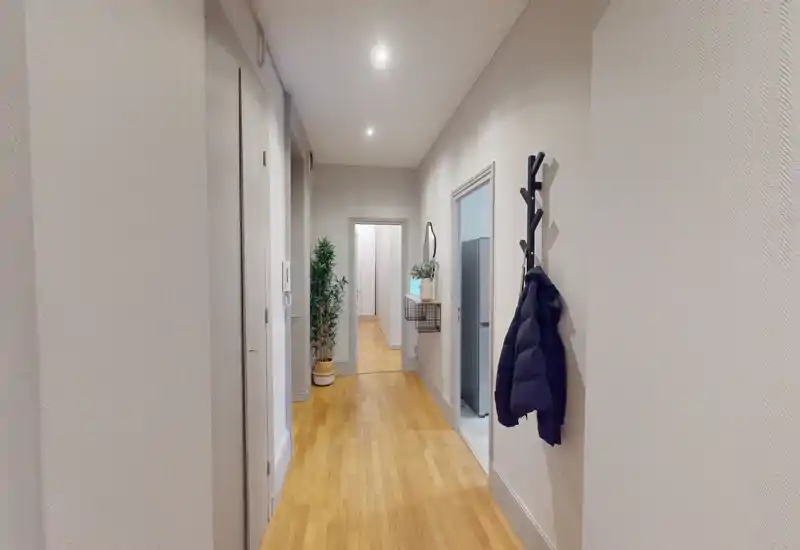 Entrée lumineuse et couloir étroit avec sol en bois, patères murales et plantes décoratives — un couloir d'accueil propre et accueillant.