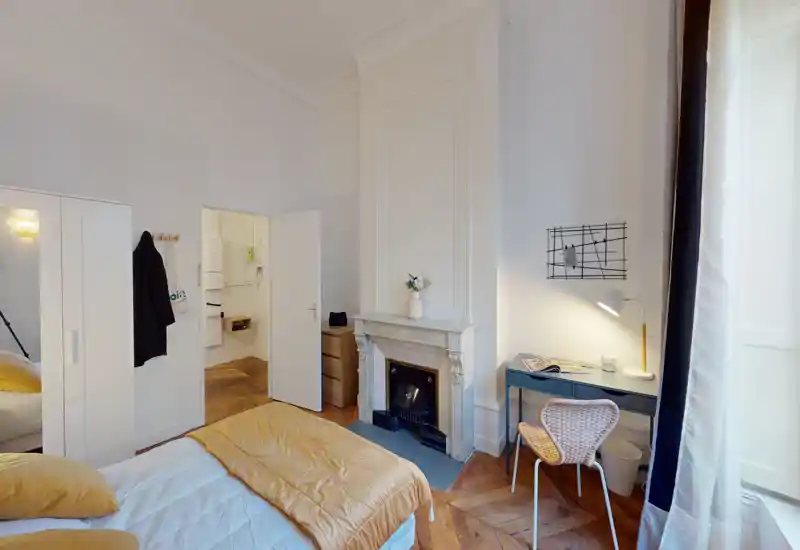 Camera da letto luminosa e raffinata con letto matrimoniale con biancheria calda, camino in marmo classico e una piccola scrivania vicino alla finestra — ideale per riposare o lavorare.