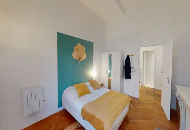 Camera da letto luminosa e accogliente con letto matrimoniale, cuscini senape e copriletto coordinato, parete d'accento verde turchese, armadio e pavimento in parquet a spina di pesce.