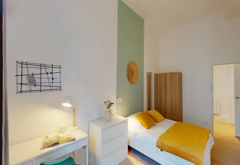 Camera da letto luminosa e ben arredata con letto matrimoniale, biancheria gialla calda, armadio e scrivania — ideale per affitti brevi che cercano un look minimal e accogliente.