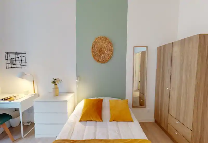 Camera da letto luminosa e ben arredata con letto centrale, cuscini color senape, trapunta bianca e armadio in legno coordinato — perfetta per un ambiente accogliente.