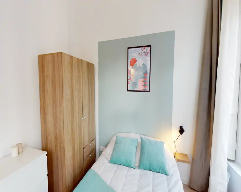 Camera da letto luminosa e ordinata con letto matrimoniale, accenti verde menta, armadio in legno e lampada da comodino vicino alla finestra — perfetta per un soggiorno accogliente.