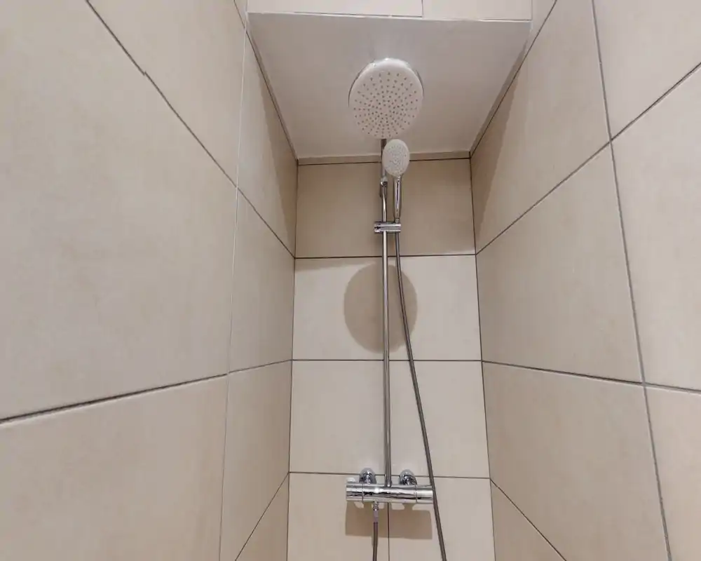 Compact tiled shower with a rainfall showerhead and handheld attachment; clean beige tiles and modern chrome fittings.