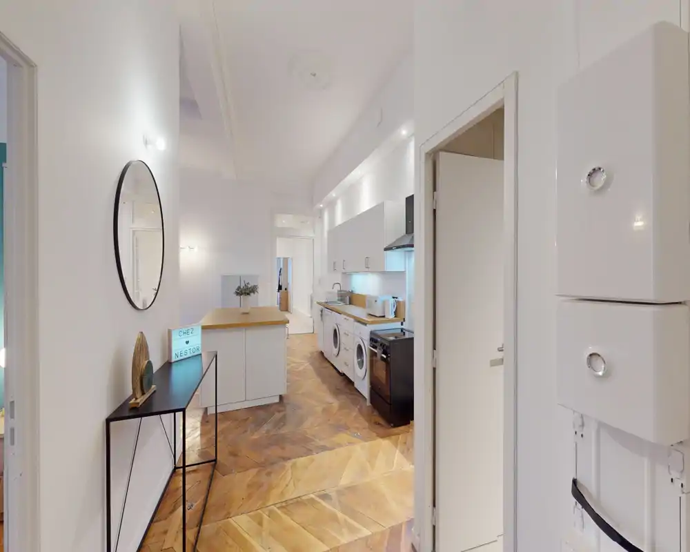 Cucina aperta e luminosa con pavimento in legno a spina di pesce, elettrodomestici integrati (lavatrice e piano cottura) e un’isola centrale per spazio di lavoro aggiuntivo.