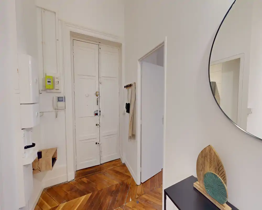 Ingresso luminoso e accogliente con porta d'ingresso a pannelli, pavimento in legno a spina di pesce e una consolle decorativa con grande specchio rotondo: uno spazio d'ingresso pratico e di stile.