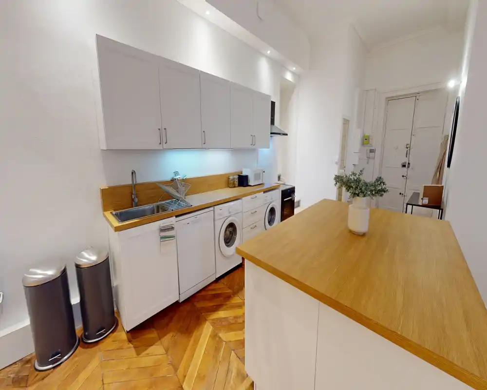 Cucina moderna a corridoio con mobili bianchi, piani in legno e pavimento in parquet; comprende lavello, lavastoviglie, lavatrice e bancone — luminosa e ben ordinata, ideale per un annuncio.