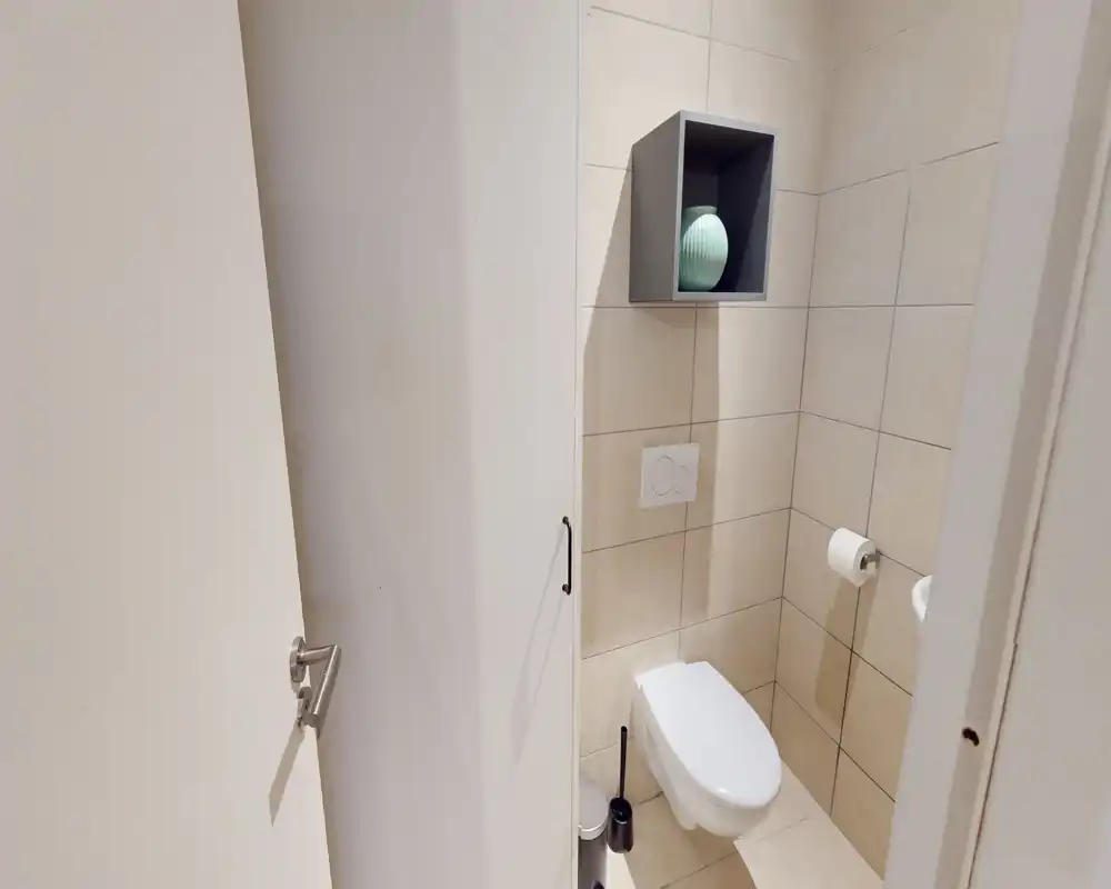 Piccolo bagno moderno con wc sospeso, pareti piastrellate e una nicchia con vaso decorativo; ambiente pulito, luminoso e compatto.
