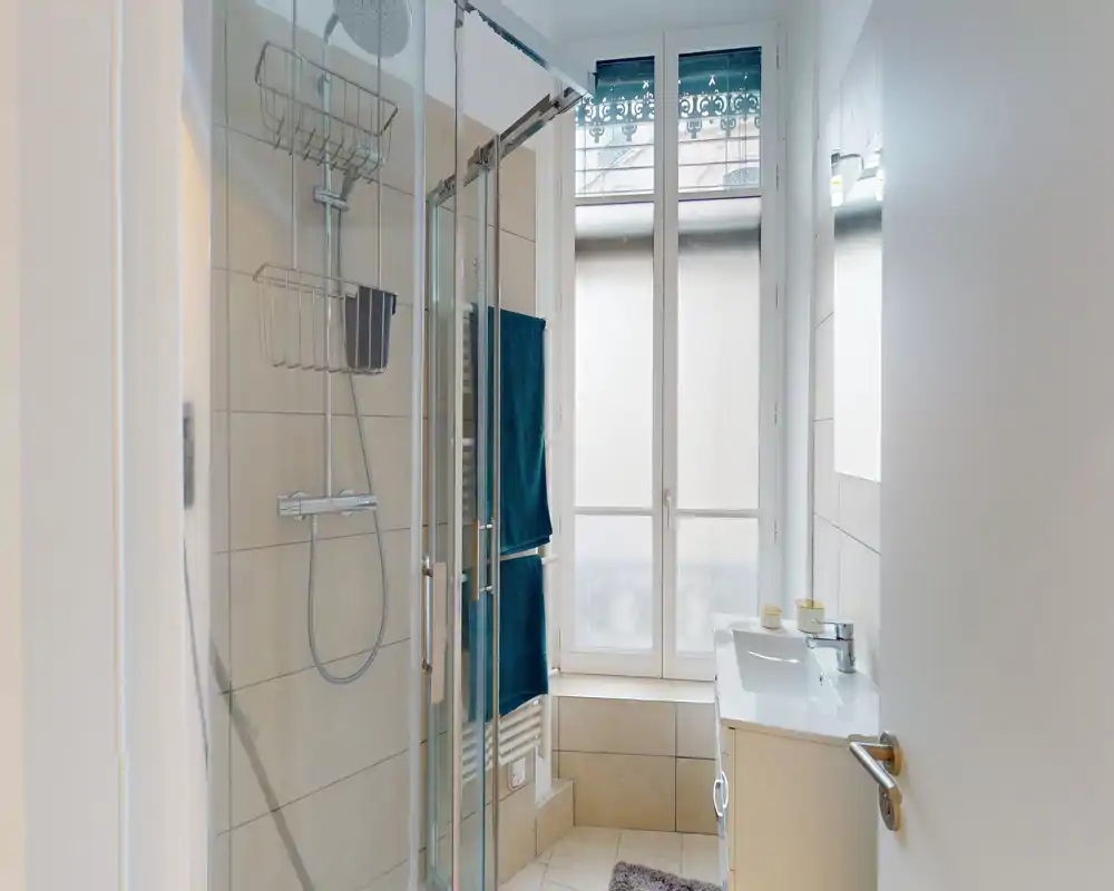 Bagno moderno e luminoso con cabina doccia in vetro, soffione a pioggia, mobile lavabo e una finestra alta satinata che garantisce luce naturale.