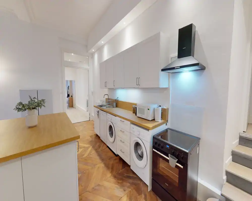 Cucina a corridoio moderna con pensili bianchi, piani in legno e elettrodomestici integrati (lavatrice/asciugatrice) e forno a libera installazione; ambiente luminoso e ben organizzato, ideale per appartamenti urbani compatti.