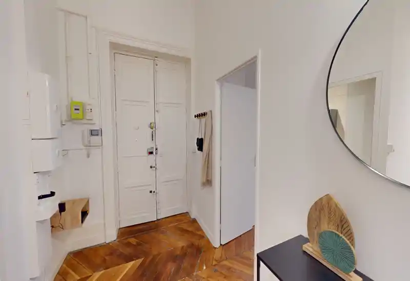 Entrée lumineuse et accueillante avec une grande porte à panneaux, un parquet point de Hongrie et une console décorative surmontée d'un miroir rond — un espace d'arrivée pratique et élégant.