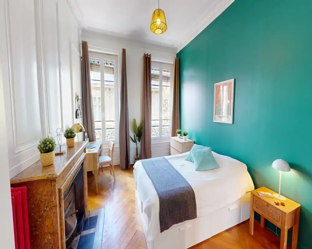 Camera da letto luminosa e di design con parete accentata turchese, letto matrimoniale comodo, pavimento in parquet e ampie finestre che garantiscono molta luce naturale.