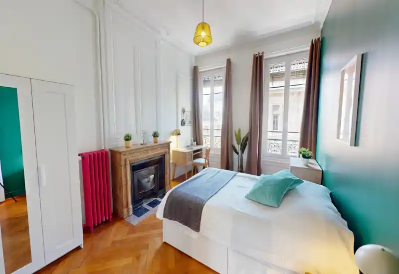 Bright, stylish bedroom with a comfortable double bed, decorative fireplace, desk by the window and warm wooden parquet flooring — ideal for a cozy city stay.