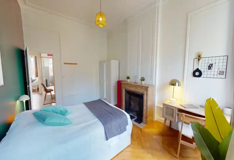 Bright, stylish bedroom with a double bed, wooden parquet, decorative cushions and a small desk beside a decorative fireplace — ideal for a comfortable city stay.