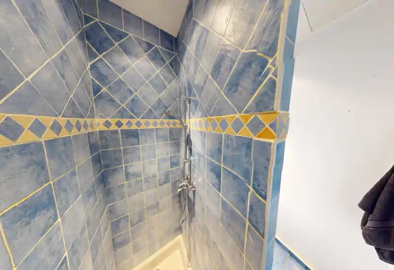 Doccia piastrellata compatta con piastrelle blu e miscelatore a parete. Rivestimento in stile mediterraneo, pulito e adatto a un bagno privato.