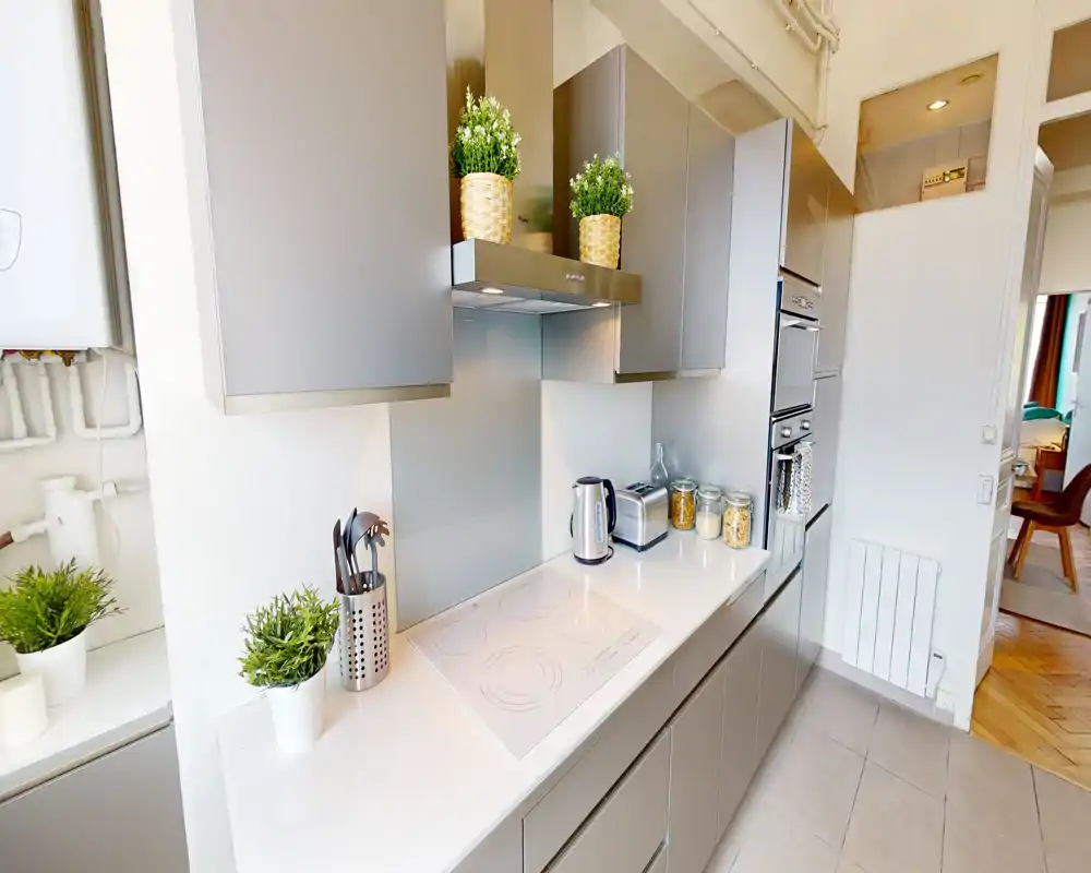 Cucina moderna e luminosa con pensili grigio elegante, piano cottura a induzione, colonne forno e piante e barattoli che donano un aspetto minimal e accogliente.