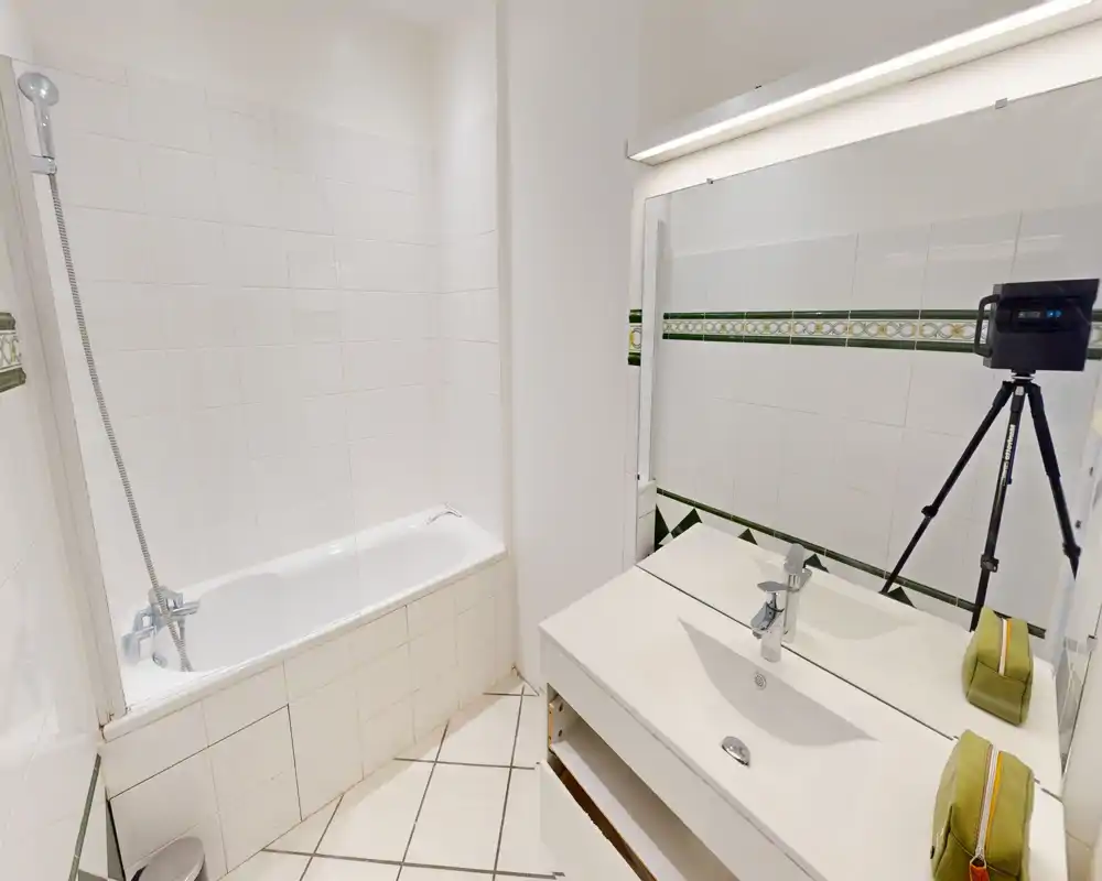 Bagno luminoso e pulito con vasca/doccia, piastrelle su pareti e pavimento, un grande specchio e un lavabo con mobile sotto.