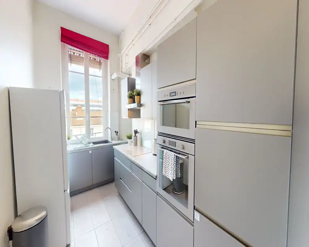 Cucina moderna a corridoio, luminosa, con mobili grigi, forno e microonde incassati, finestra che porta luce naturale e layout compatto ed efficiente.