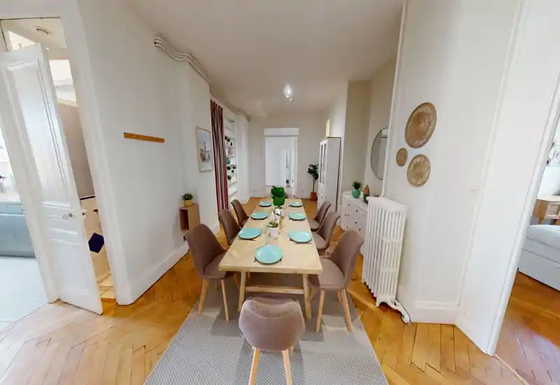 Bright, styled dining room with a large wooden table set for eight, comfortable upholstered chairs and tasteful décor — ideal for shared meals.