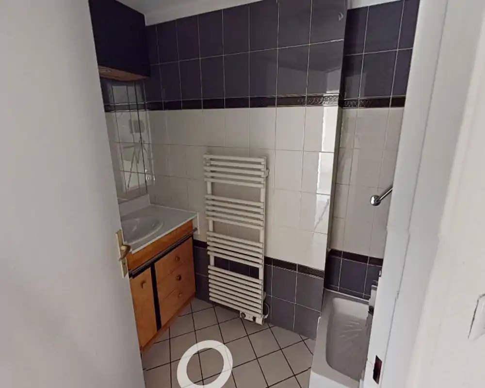 Petit salle de bain carrelée avec lavabo et meuble, miroir, porte-serviettes chauffant et vue partielle du receveur de douche; tons neutres et équipements pratiques.