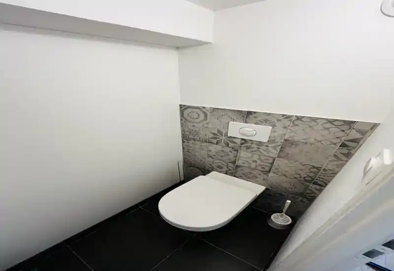 Bagno compatto e moderno con wc sospeso, piastrelle decorative sul muro e pavimento scuro. Design essenziale ideale per un piccolo bagno per gli ospiti.