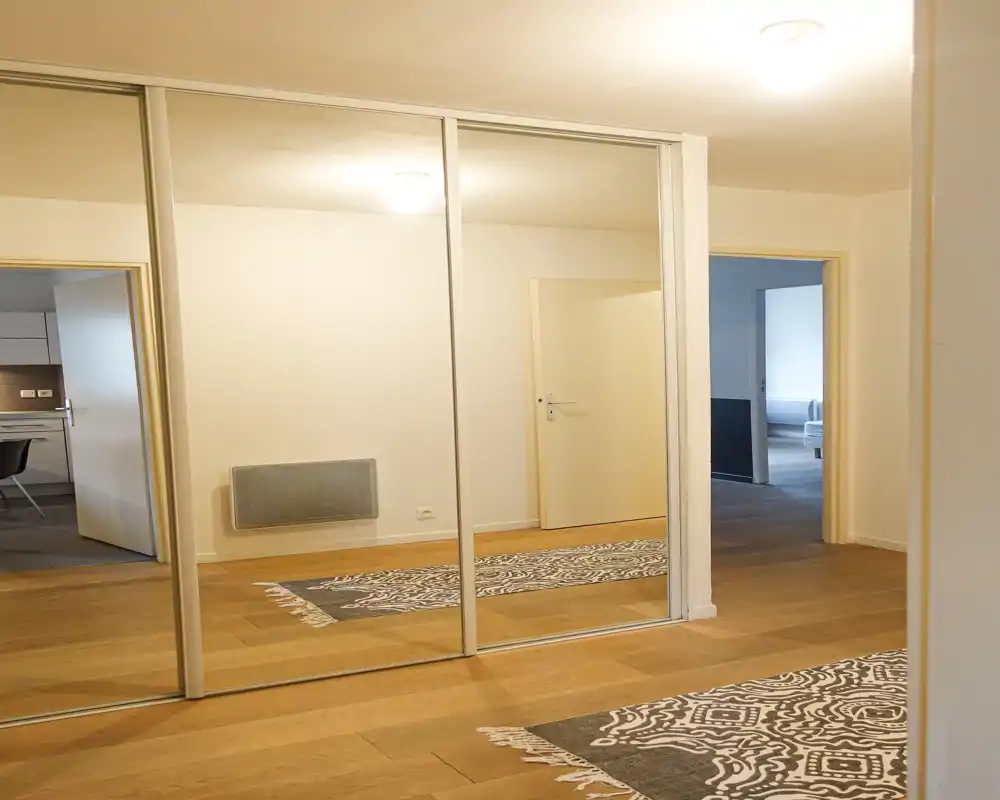 Entrée/couloir lumineux et minimaliste avec parquet en bois et grands placards encastrés à portes miroir reflétant les pièces adjacentes.