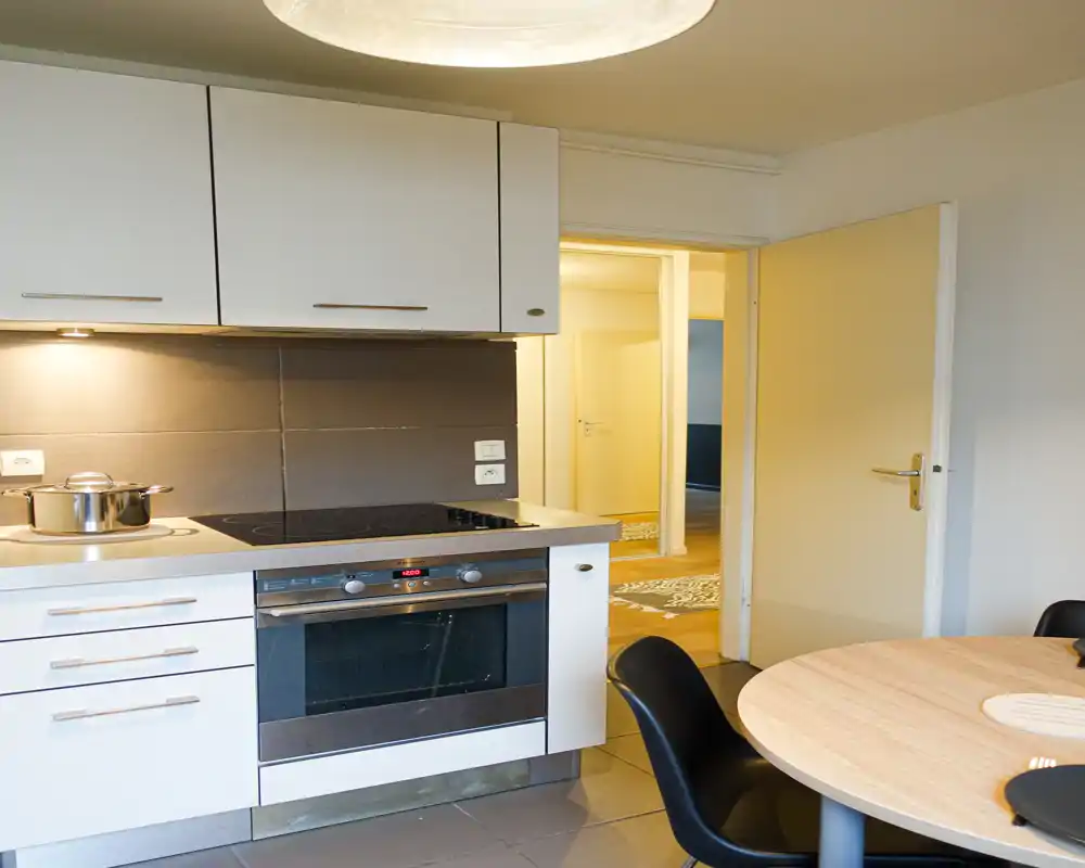 Cuisine compacte et moderne avec four encastré, plaque à induction et petite table ronde — lumineuse, soignée et prête à l'emploi.