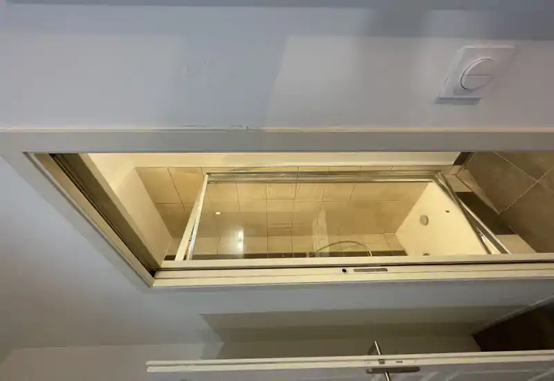 Ducha compacta con paredes alicatadas y puerta corredera de vidrio; cabina luminosa y limpia, adecuada para un anuncio.