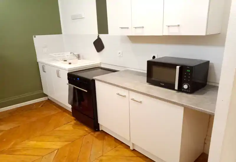 Cocina compacta y moderna con muebles blancos, placa independiente, microondas y suelo de parquet que aporta calidez.
