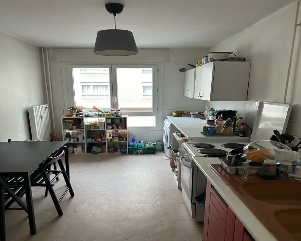 Ampia zona giorno/pranzo con un tavolo centrale e luce naturale da due finestre; la stanza è abitata con oggetti disposti e sedie intorno al tavolo.
