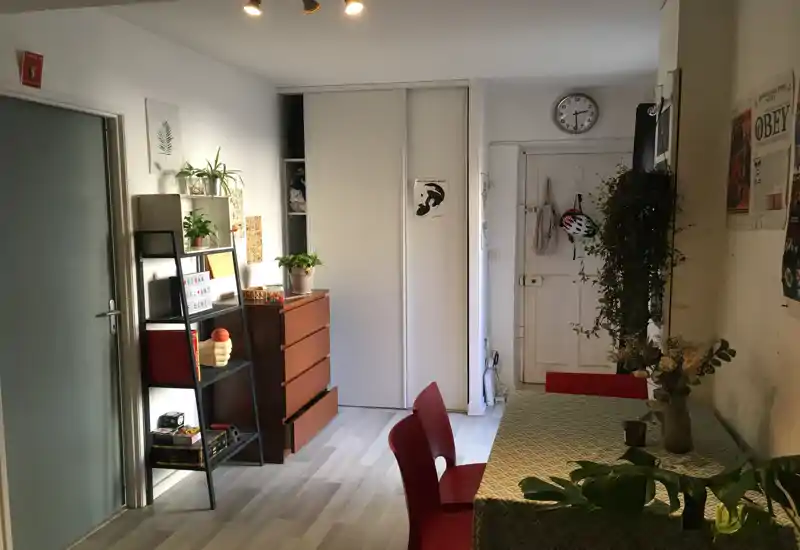 Cozy dining area with a table covered by a patterned cloth, red chairs and plants; bright, lived-in space ideal for meals or working at the table.