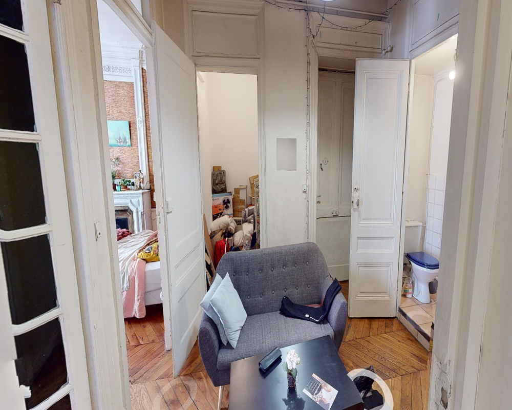 Espace salon confortable avec canapé deux places, table basse et parquet en chevrons; la photo montre l'espace de vie et ses connexions vers les pièces attenantes.