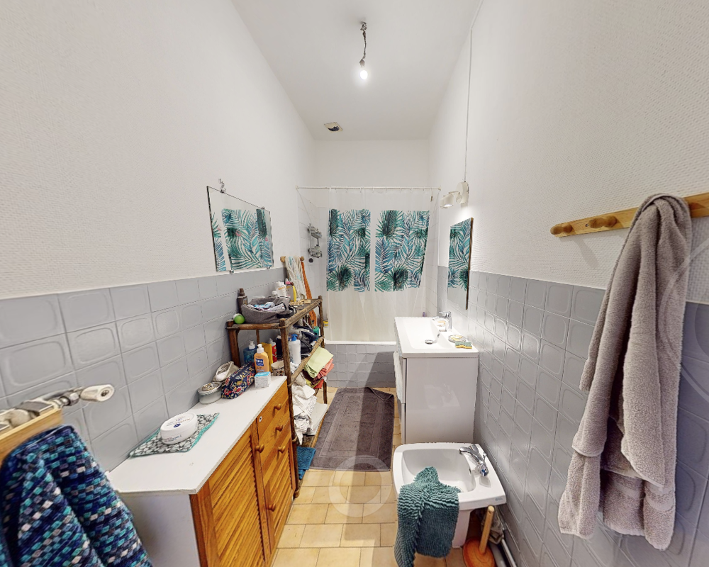 Baño equipado con lavabo, bidé y cortina de ducha, azulejos neutros y acentos verde azulado para un aspecto fresco.