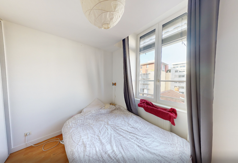 Small, bright bedroom with a double bed by a large window; simple, clean décor and natural light.