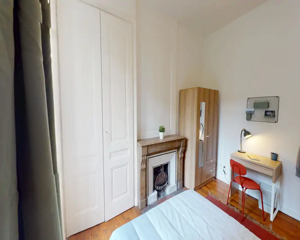Camera da letto luminosa e ordinata con letto visibile, pavimento in legno, piccolo scrittoio e armadio — ideale per un single o soggiorni brevi.